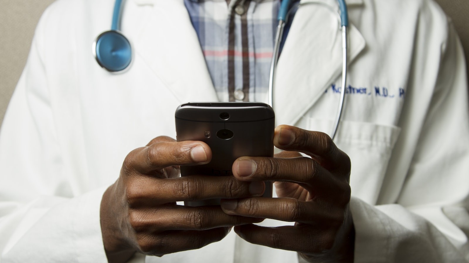 Physician in a white coat with a stethoscope typing on a smartphone